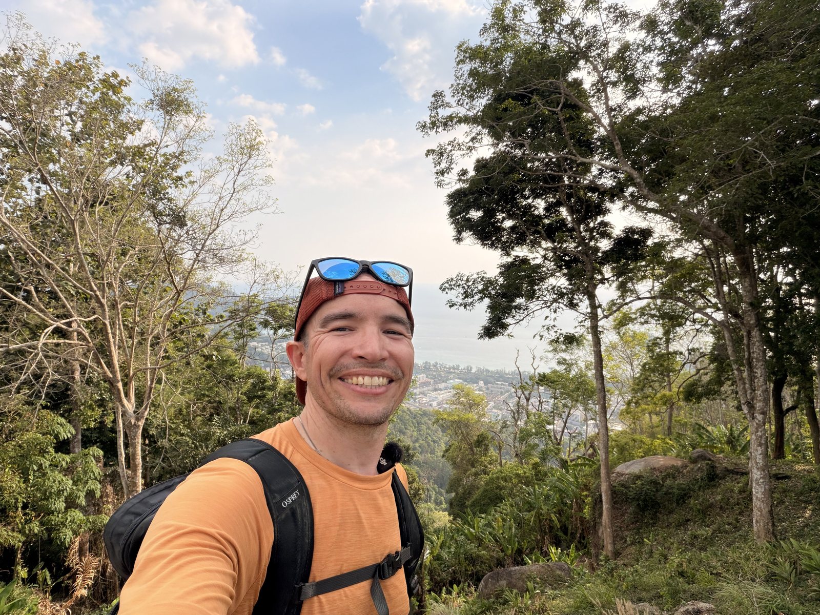 Joe on a trail above the coast, pack on, sunglasses on his cap